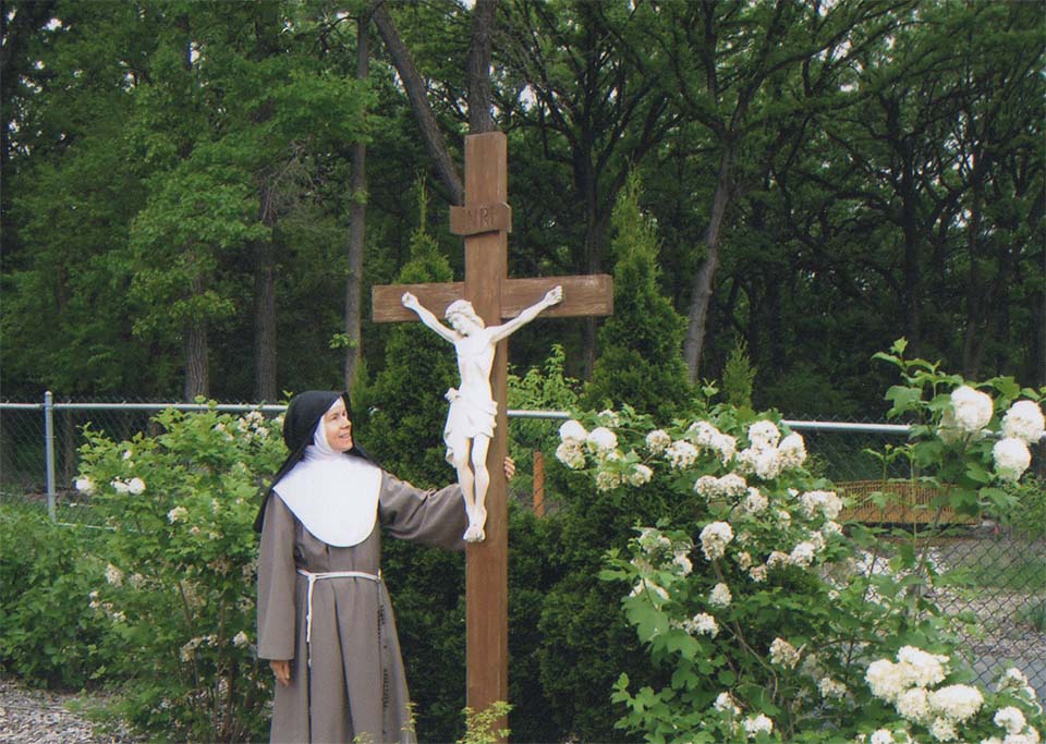 Nun standing at crucifix in the center of the garden.